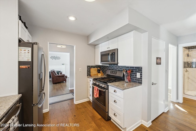 kitchen with white cabinets, decorative backsplash, light wood-type flooring, light stone countertops, and stainless steel appliances