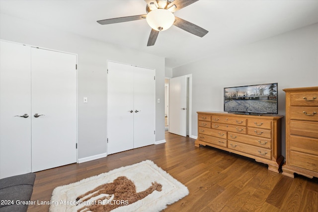 bedroom featuring ceiling fan, dark hardwood / wood-style flooring, and two closets