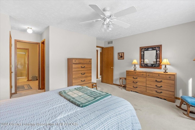 bedroom featuring ceiling fan, ensuite bathroom, light carpet, and a textured ceiling