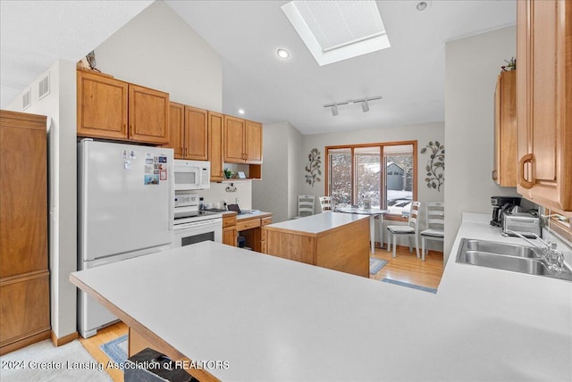 kitchen with sink, white appliances, kitchen peninsula, a skylight, and a kitchen island