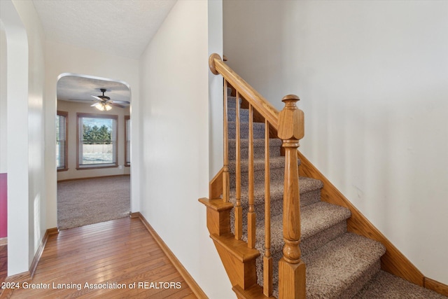 stairway with ceiling fan, a textured ceiling, and hardwood / wood-style flooring