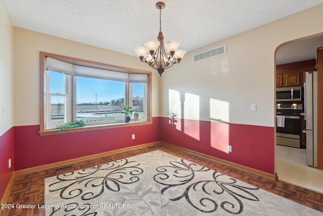 empty room with dark parquet flooring, a textured ceiling, and a notable chandelier