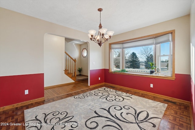 empty room with dark parquet floors and a notable chandelier