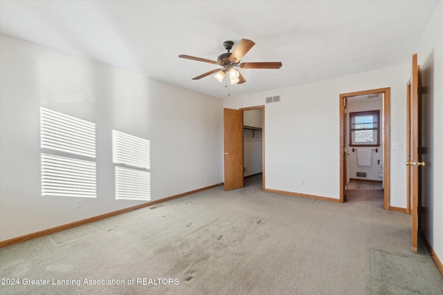 unfurnished bedroom featuring ceiling fan, a walk in closet, light carpet, and a closet