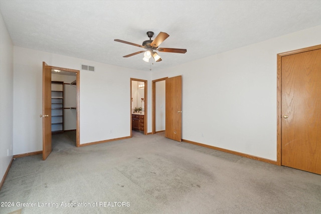 unfurnished bedroom with ensuite bath, ceiling fan, light colored carpet, a walk in closet, and a closet