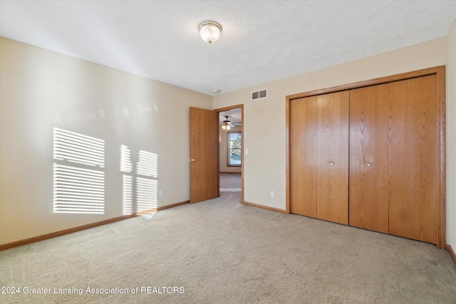 unfurnished bedroom with light colored carpet, a textured ceiling, and a closet