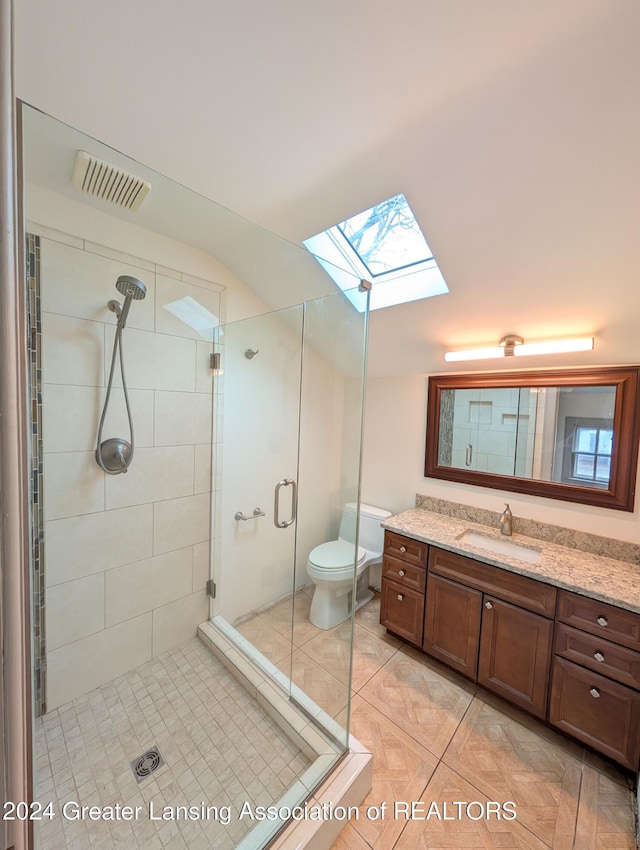 bathroom with toilet, vanity, tile patterned flooring, a shower with shower door, and a skylight