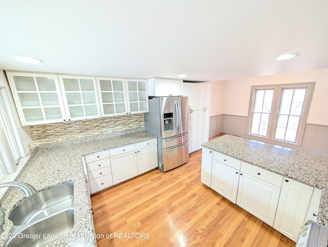 kitchen featuring stainless steel refrigerator with ice dispenser, sink, white cabinetry, and light stone counters