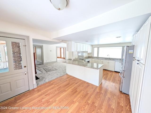 kitchen with kitchen peninsula, sink, white cabinets, stainless steel fridge, and light stone counters