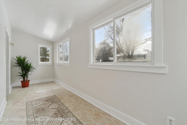 hall featuring a healthy amount of sunlight, light tile patterned flooring, and vaulted ceiling