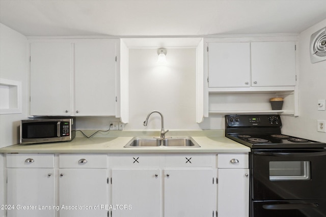 kitchen featuring black range with electric stovetop, white cabinetry, and sink