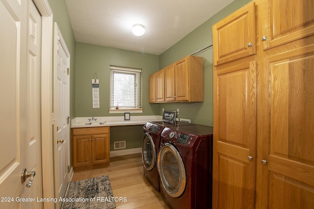 laundry room featuring washing machine and dryer, light wood-type flooring, and cabinets