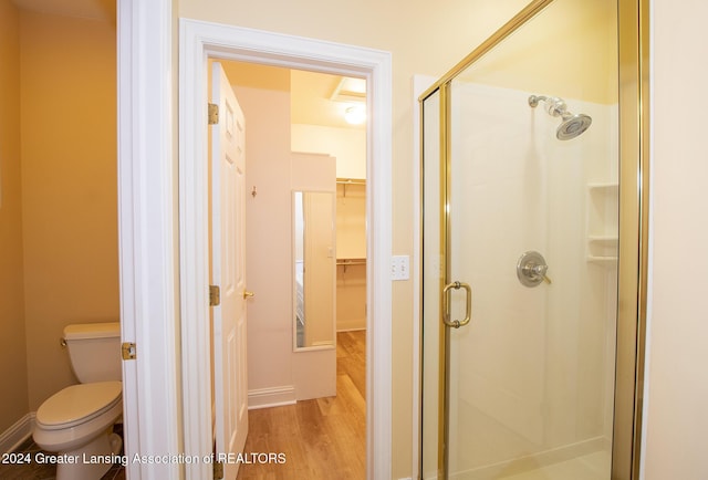 bathroom with toilet, a shower with door, and wood-type flooring