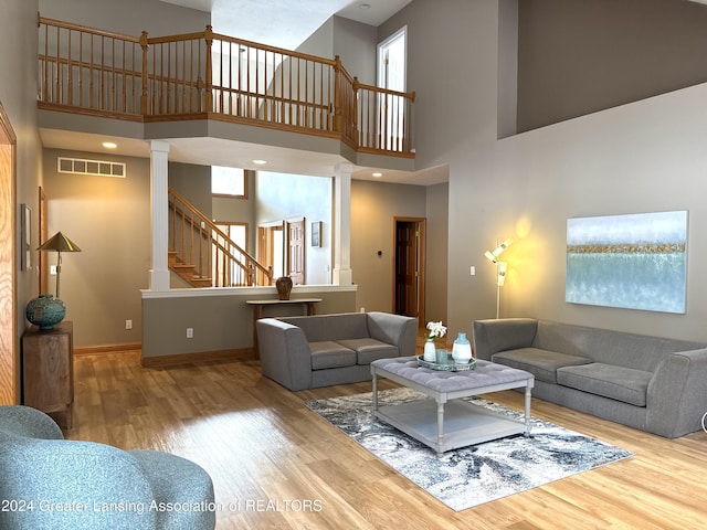 living room with a high ceiling, decorative columns, a healthy amount of sunlight, and hardwood / wood-style floors