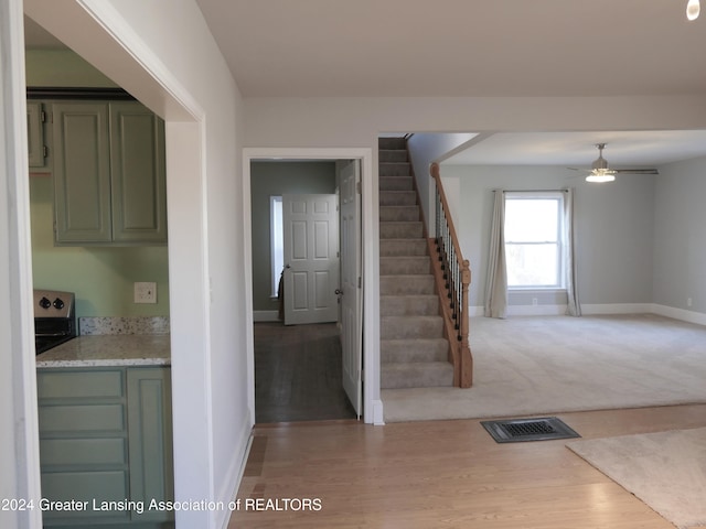 interior space with ceiling fan, green cabinets, light colored carpet, and light stone counters