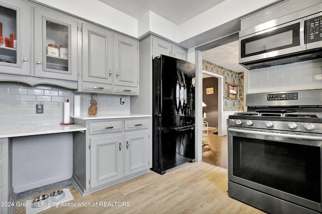 kitchen with tasteful backsplash, stainless steel appliances, gray cabinets, and light hardwood / wood-style flooring