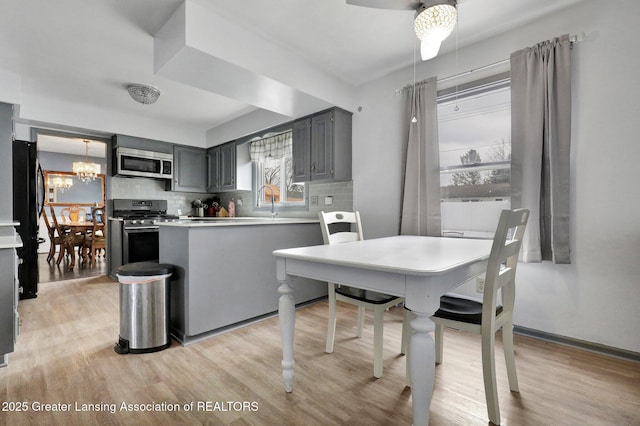 kitchen featuring gray cabinetry, backsplash, a notable chandelier, stainless steel appliances, and light wood-type flooring