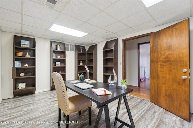 office featuring a drop ceiling, wood-type flooring, and built in shelves