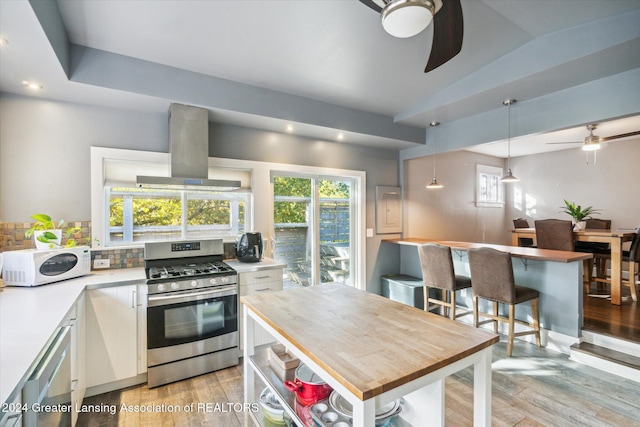 kitchen with island exhaust hood, pendant lighting, white cabinets, and stainless steel appliances