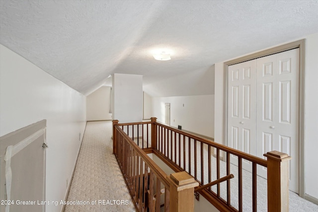 corridor featuring a textured ceiling, light colored carpet, and lofted ceiling