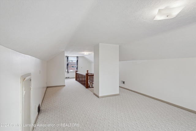 bonus room with a textured ceiling, light colored carpet, and vaulted ceiling