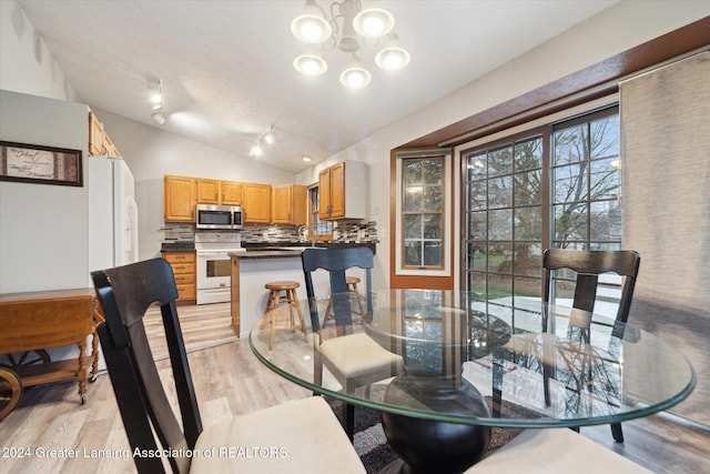 dining space featuring a notable chandelier, light wood-type flooring, vaulted ceiling, and sink