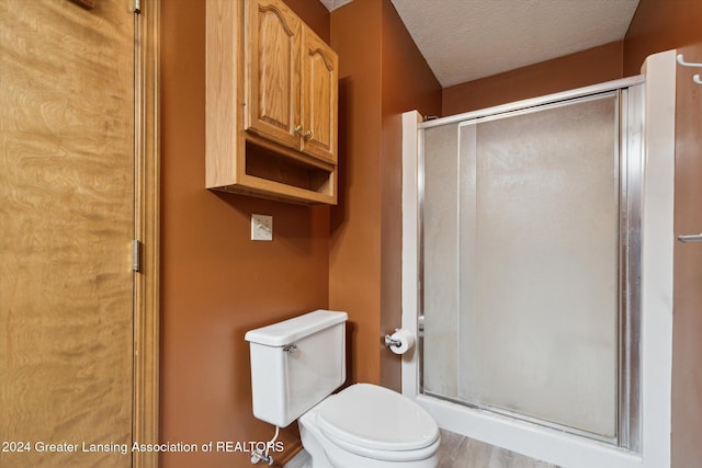 bathroom with toilet, an enclosed shower, and a textured ceiling