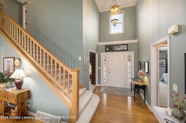 foyer with a chandelier, a towering ceiling, light hardwood / wood-style flooring, and ornamental molding