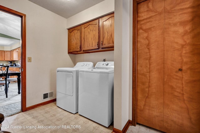 clothes washing area with washing machine and dryer, cabinets, and a textured ceiling