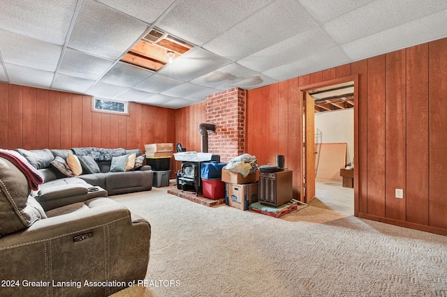 carpeted living room featuring a wood stove, a drop ceiling, and wood walls