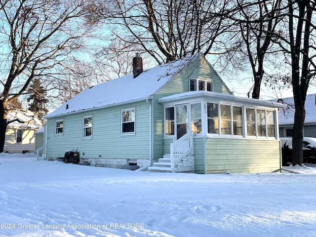 snow covered back of property featuring a sunroom