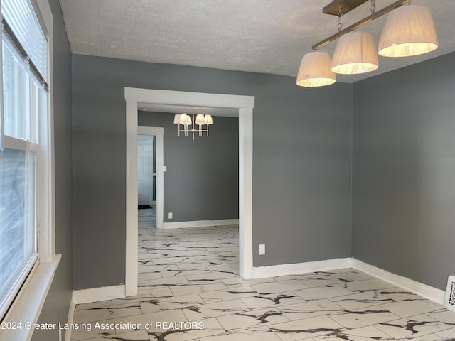 unfurnished room with a notable chandelier and a textured ceiling