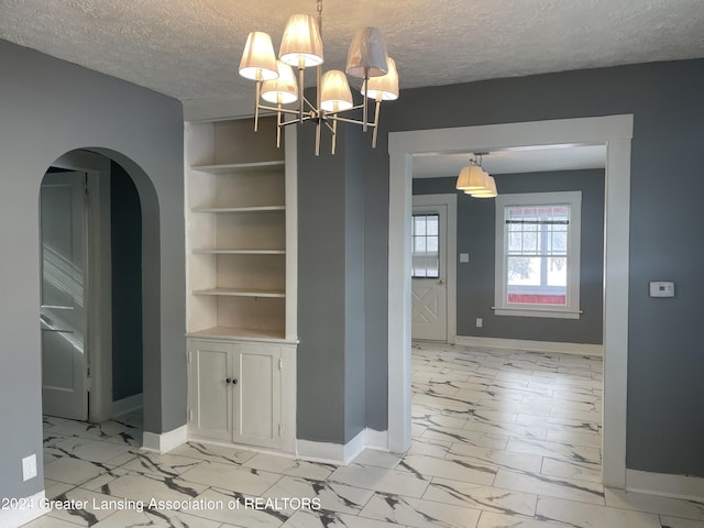 unfurnished dining area with built in shelves, a textured ceiling, and a chandelier