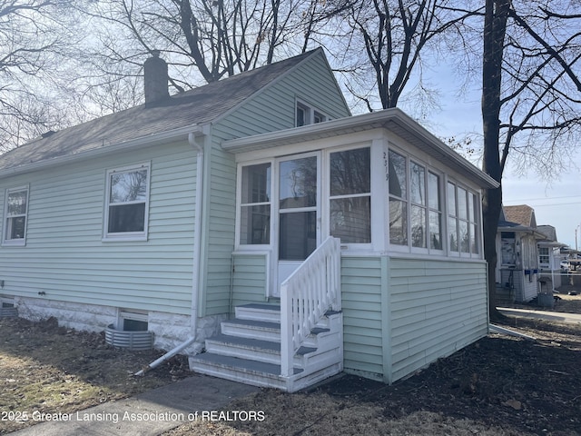 view of front of house featuring entry steps, roof with shingles, a sunroom, and a chimney