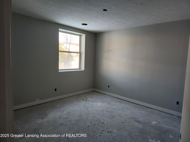 spare room with baseboards, concrete flooring, and a textured ceiling