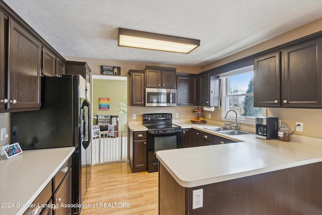 kitchen with kitchen peninsula, dark brown cabinets, black appliances, light hardwood / wood-style flooring, and sink