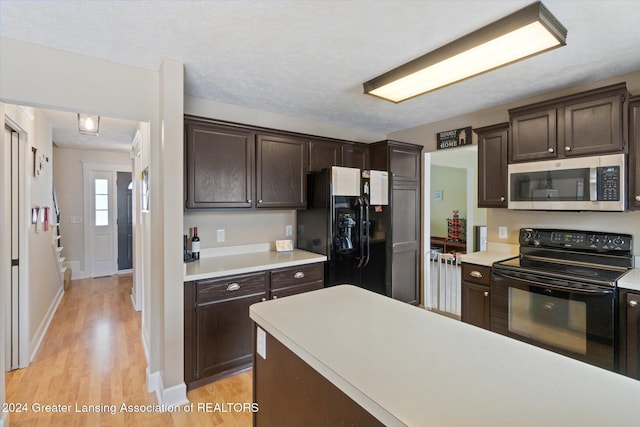 kitchen with a textured ceiling, dark brown cabinetry, black appliances, and light hardwood / wood-style flooring