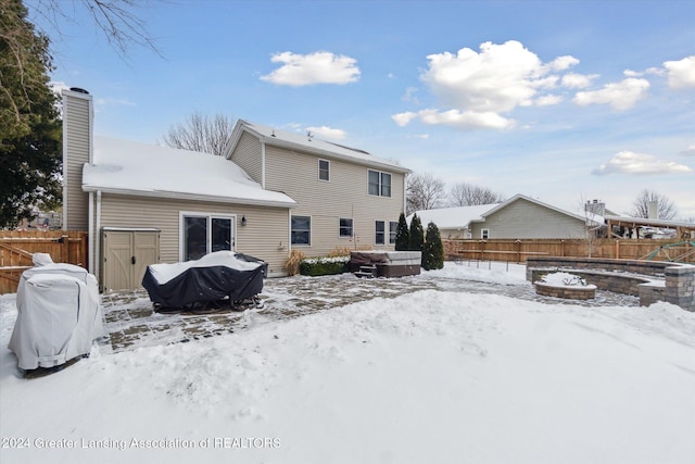 snow covered house featuring a hot tub and a fire pit