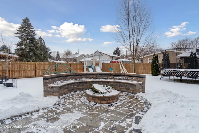 snow covered patio with a trampoline, a fire pit, and a playground