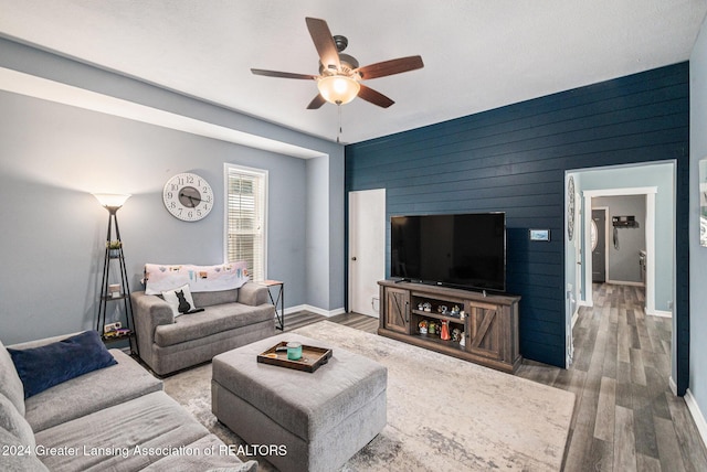 living room featuring wood-type flooring, ceiling fan, and wood walls