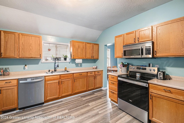 kitchen featuring sink, light hardwood / wood-style floors, a textured ceiling, lofted ceiling, and appliances with stainless steel finishes