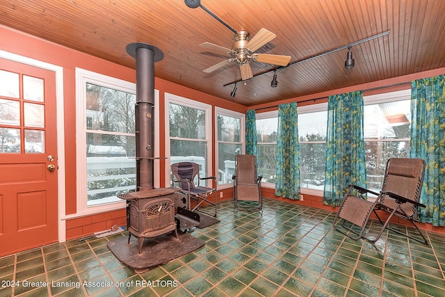 sunroom with ceiling fan, track lighting, a wood stove, and wooden ceiling