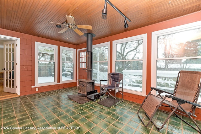 sunroom / solarium featuring ceiling fan, a wood stove, and rail lighting