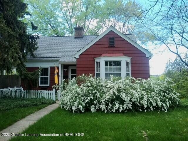 bungalow-style house with a front lawn, fence, roof with shingles, and a chimney