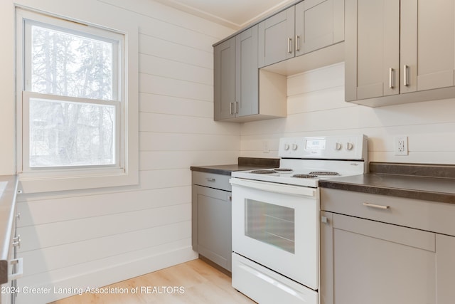 kitchen featuring gray cabinetry, light hardwood / wood-style floors, white range oven, and wood walls