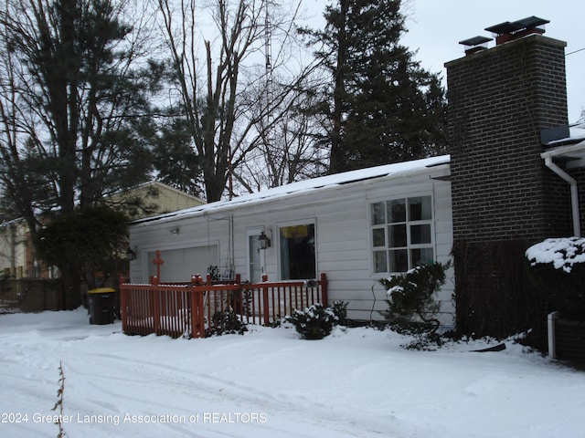 snow covered back of property featuring a garage