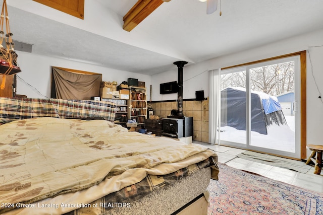 bedroom with access to outside, ceiling fan, a wood stove, and beamed ceiling