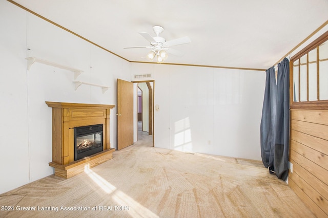 unfurnished living room featuring crown molding, carpet floors, wooden walls, and ceiling fan