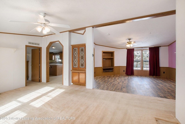 unfurnished living room featuring wooden walls, carpet floors, ornamental molding, ceiling fan, and a textured ceiling