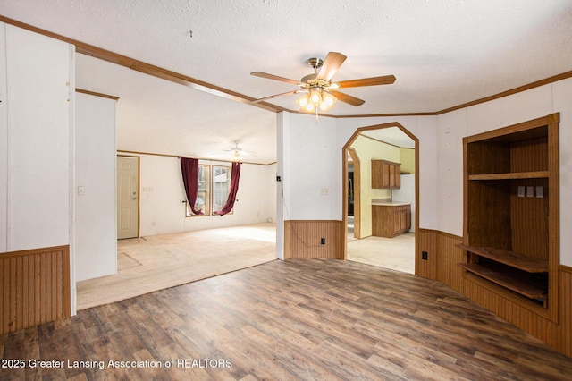 unfurnished living room featuring a textured ceiling, ornamental molding, ceiling fan, and light wood-type flooring